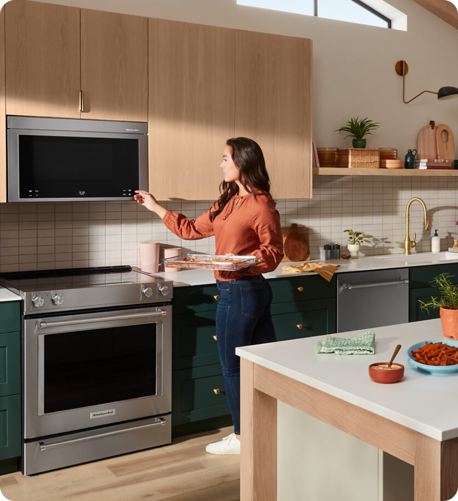 Cocina moderna con electrodomésticos KitchenAid, Maytag, Whirlpool y Acros. Mujer cocinando en una cocina elegante con electrodomésticos de alta calidad.